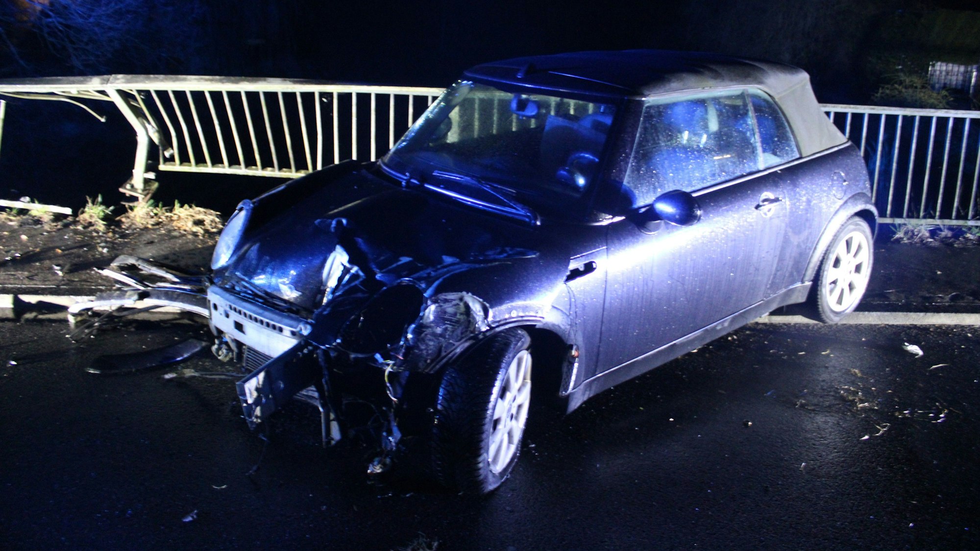 Ein verunfallter Mini steht auf einer Brücke an einem schwer beschädigten Brückengeländer in Rösrath-Lehmbach.