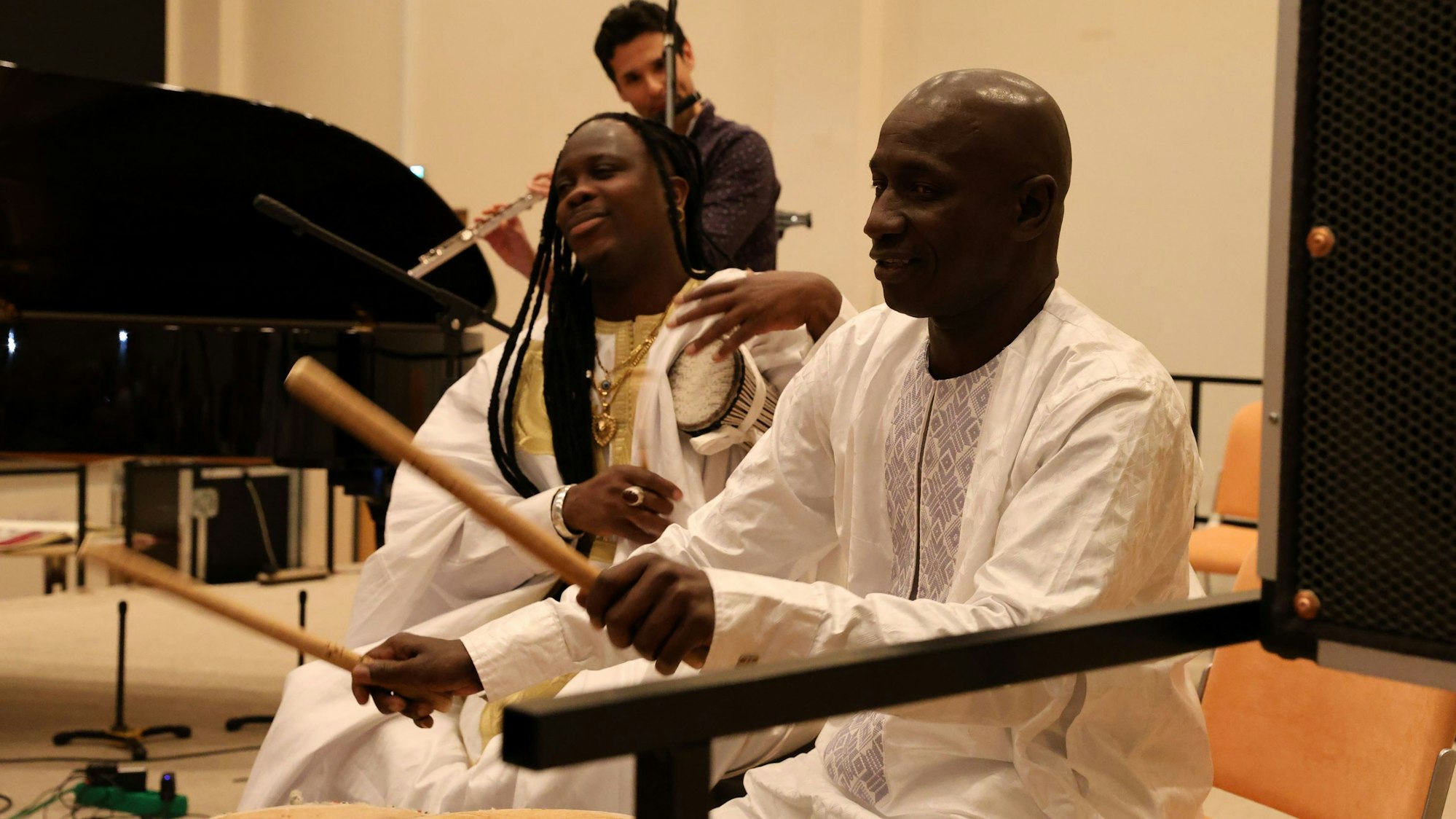 Zwei Männer und eine Frau musizieren an Trommeln und an einer Querflöte.