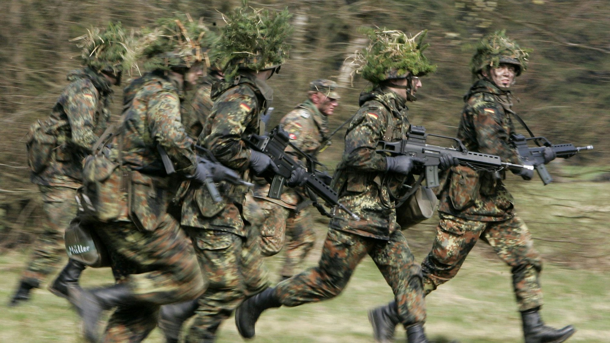 Mit Blattwerk und Gras getarnte Wehrpflichtige von den Panzergrenadieren rennen mit ihren Waffen im Rahmen ihrer Grundausbildung bei einer Übung über das freie Gelände der Knüll Kaserne in Schwarzenborn (Schwalm-Eder-Kreis).