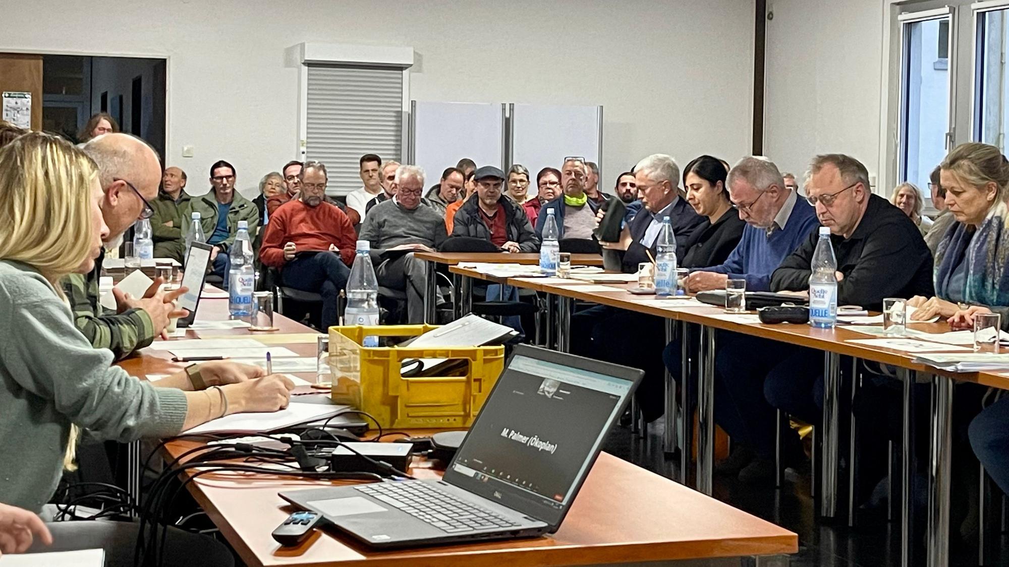 Männer und Frauen sitzen an langen Tischen.