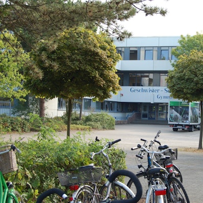 Zu sehen ist ein Schulgebäude mit einer Fassade, auf dem Schulhof stehen Fahrräder.