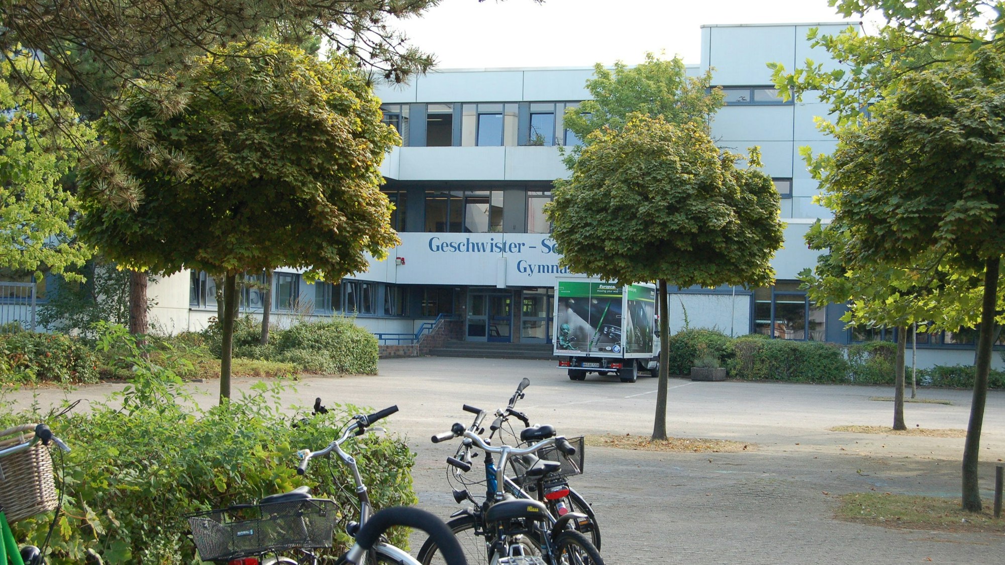 Zu sehen ist ein Schulgebäude mit einer Fassade, auf dem Schulhof stehen Fahrräder.