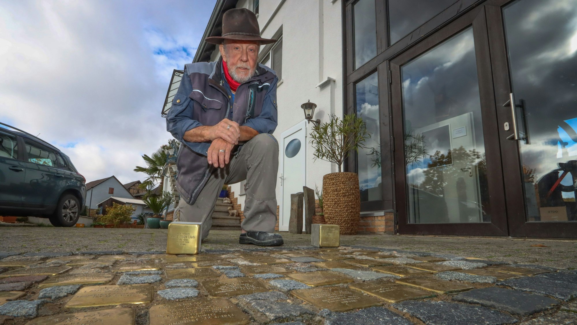 Künstler Gunter Demnig arbeitet goldene Stolpersteine in das Pflaster einer Straße ein.