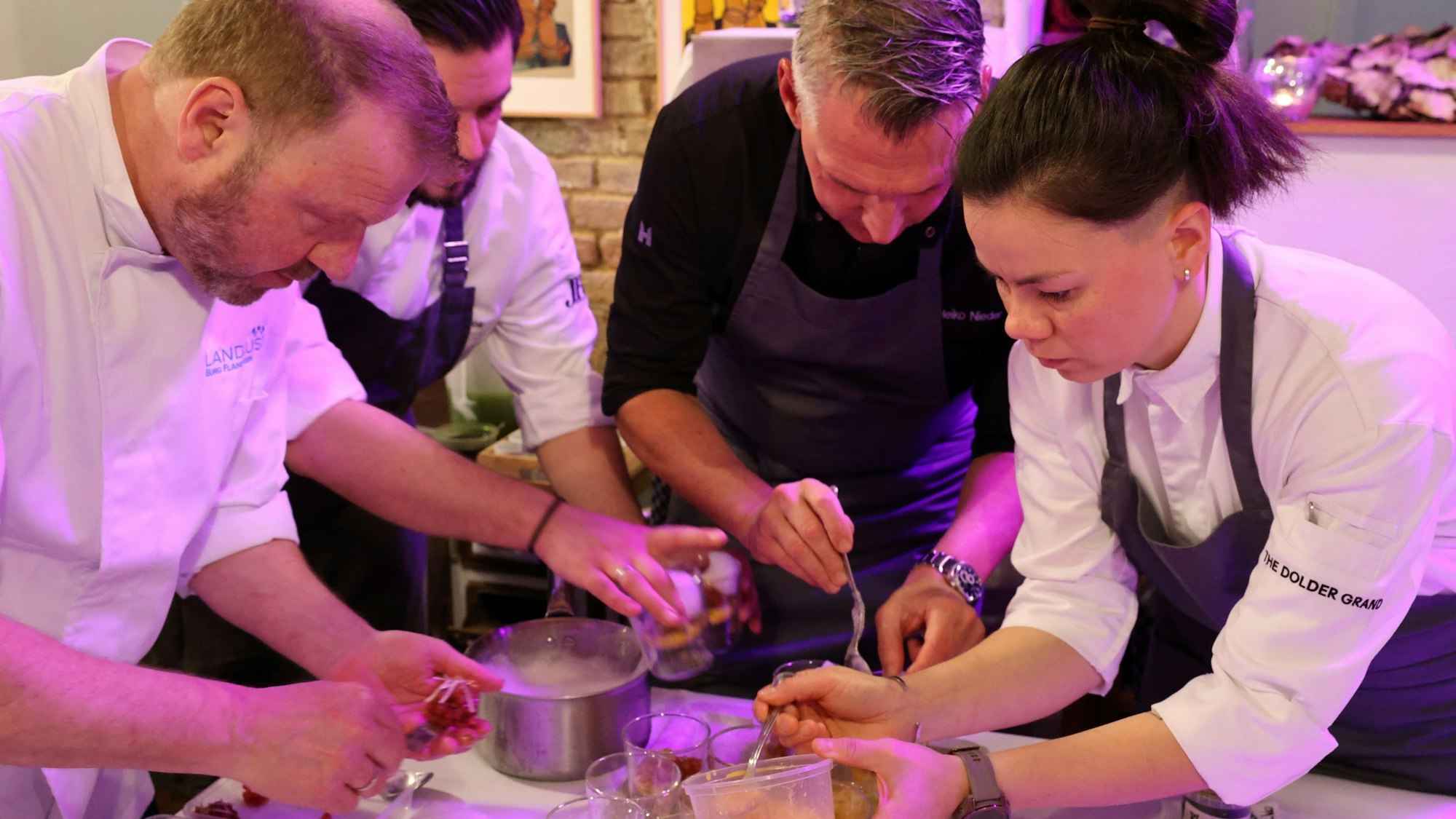 Die drei Köche und die Köchin stehen im Halbkreis und richten Teller mit dem Gruß aus der Küche an.