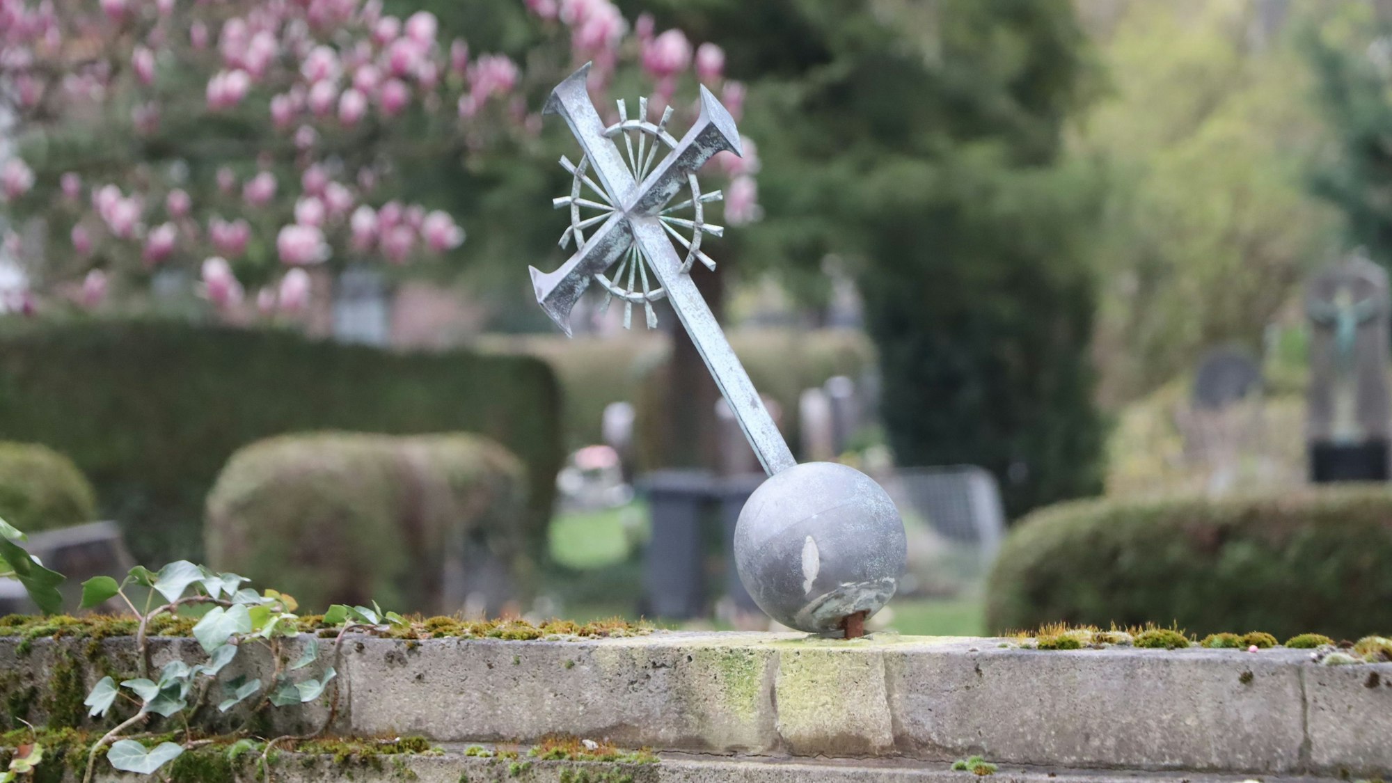 Auf dem Foto ist ein Metallkreuz zu sehen, das so gerade eben noch von seiner Verankerung gehalten wird.