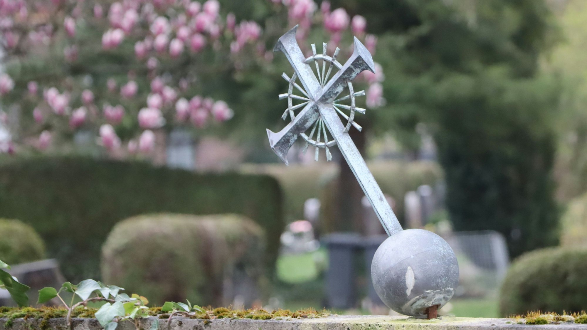 Das Bild zeigt ein verbogenes Kreuz auf einem Friedhof.