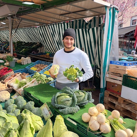 Mann an einem Marktstand mit Gemüse in der Hand
