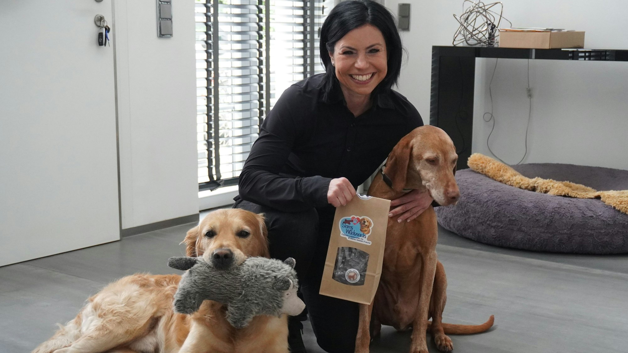 Ein Frau kniet lächelnd neben zwei Hunden.