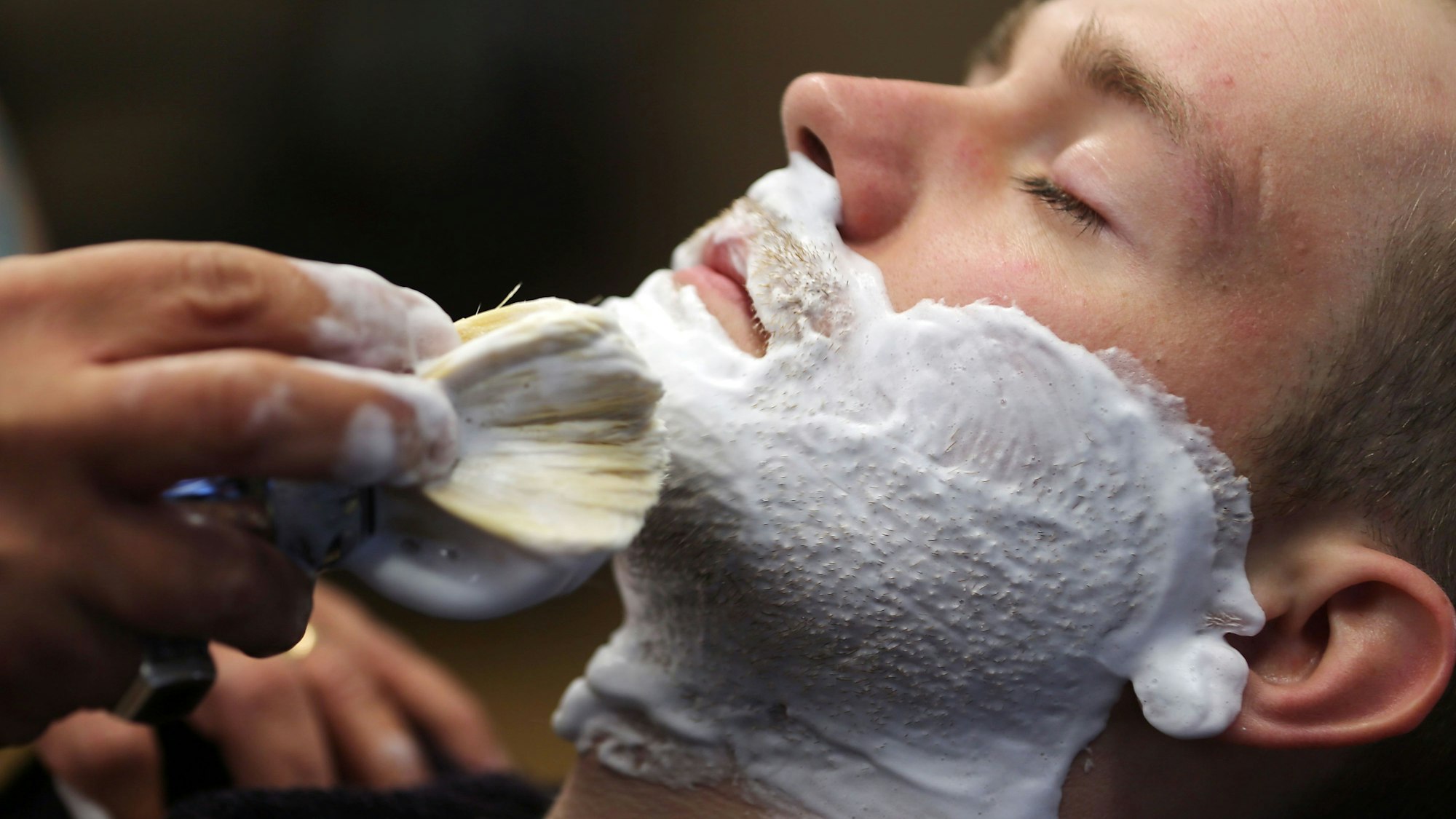 Ein Barbier seift seinen Kunden ein.