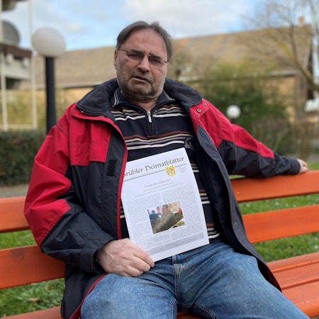 Zu sehen ist ein Mann, der auf einer roten Parkbank sitzt.