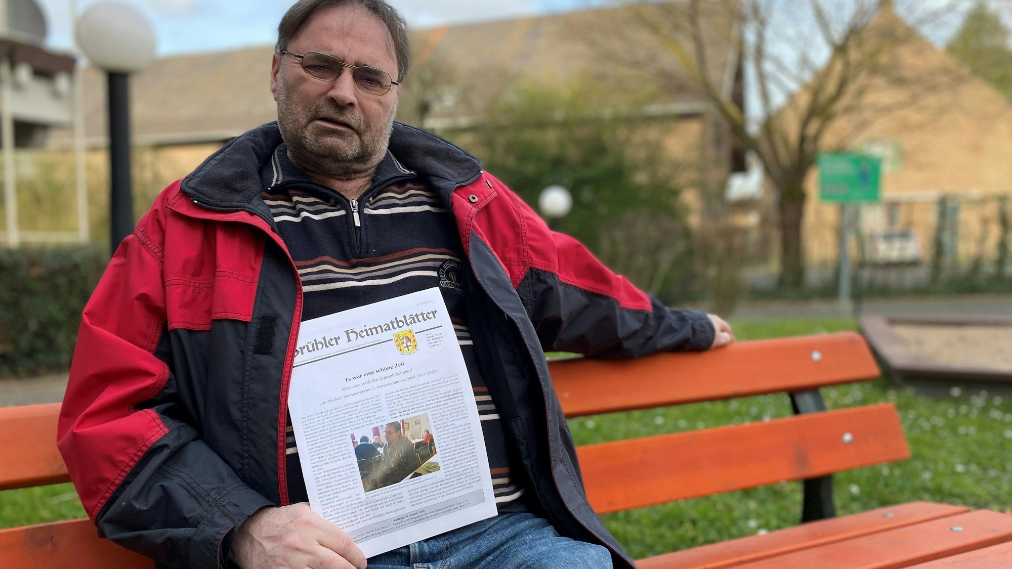 Zu sehen ist ein Mann, der auf einer roten Parkbank sitzt.