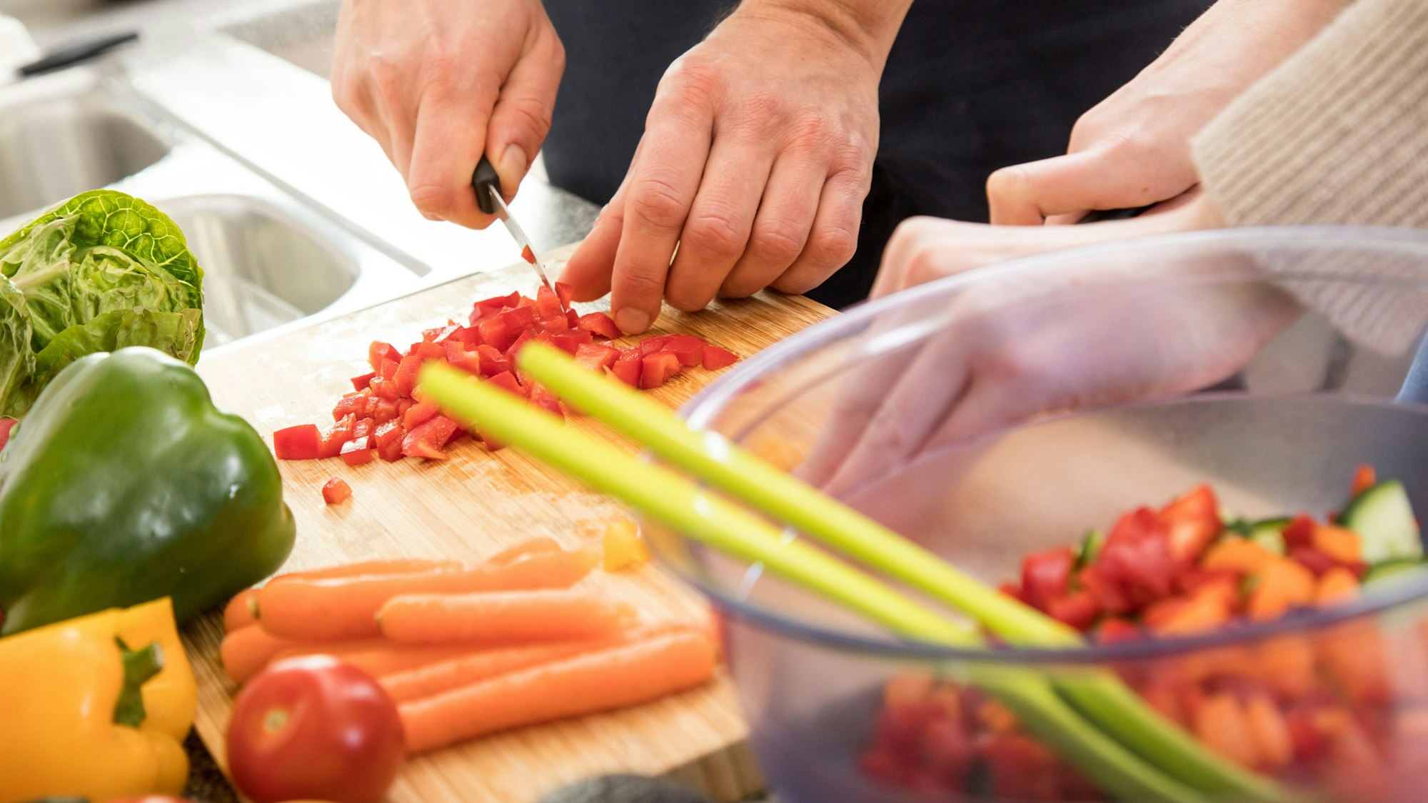 Zwei Personen schneiden Gemüse auf einem Schneidebrett.