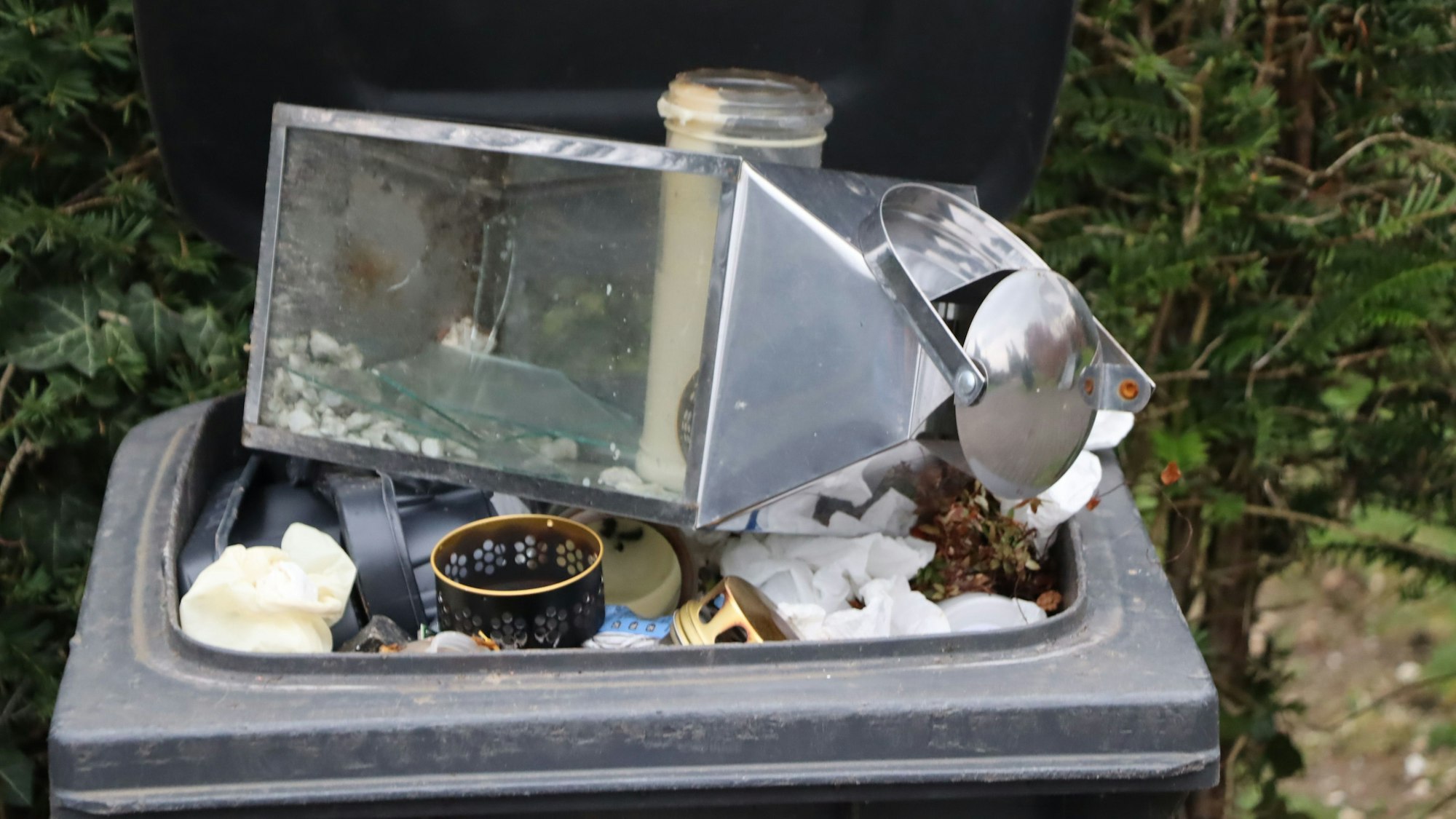 Auf dem Foto ist ein Mülleimer zu sehen, in dem zerstörte Grabutensilien liegen.
