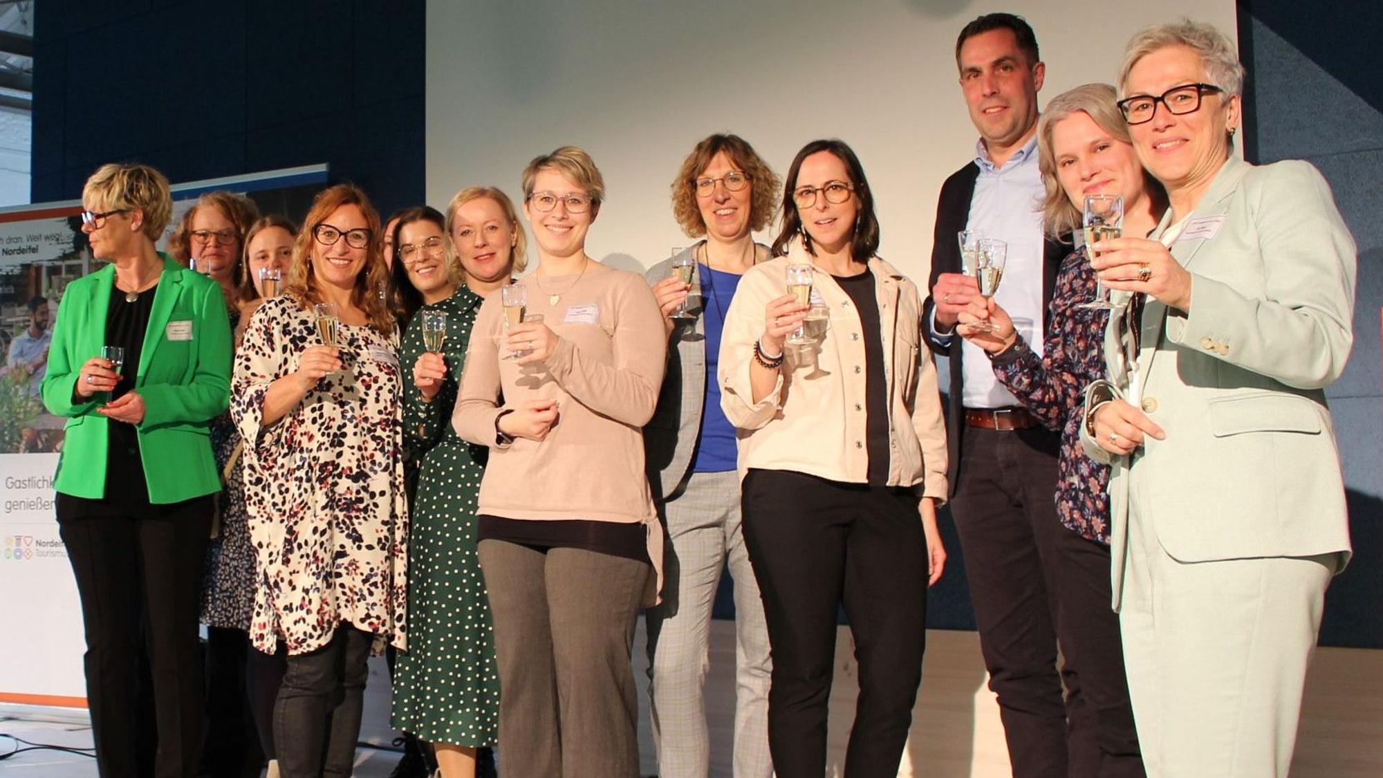 Das Team der Nordeifel Tourismus steht auf der Bühne und prostet den Gästen zu.