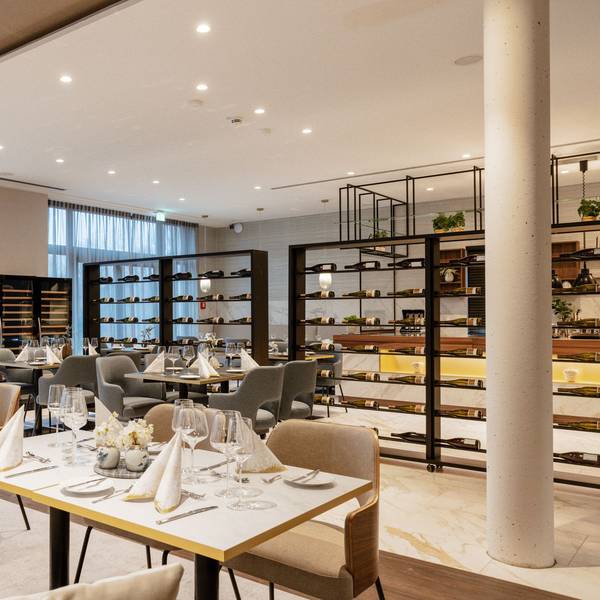 Zu sehen ist ein helles Restaurant mit gedeckten Tischen und Weinregalen.