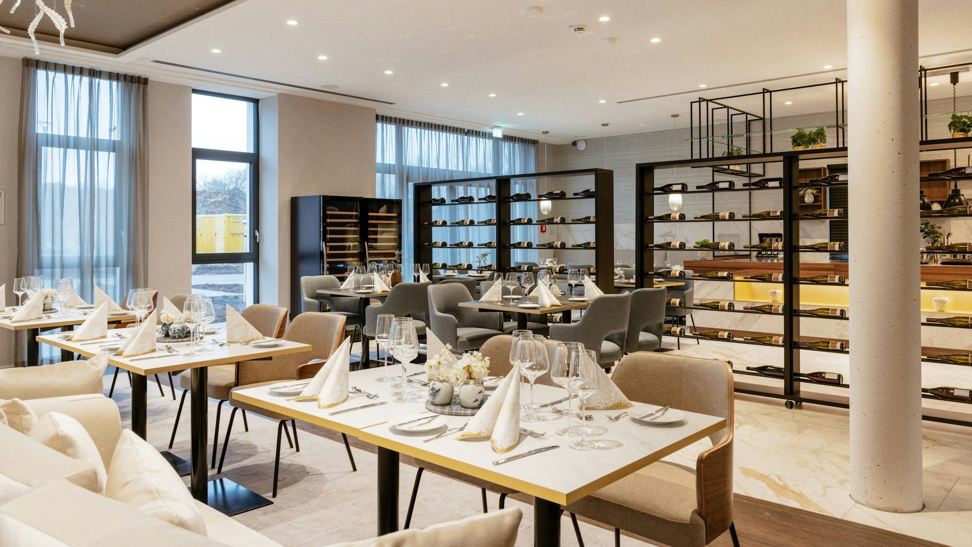 Zu sehen ist ein helles Restaurant mit gedeckten Tischen und Weinregalen.