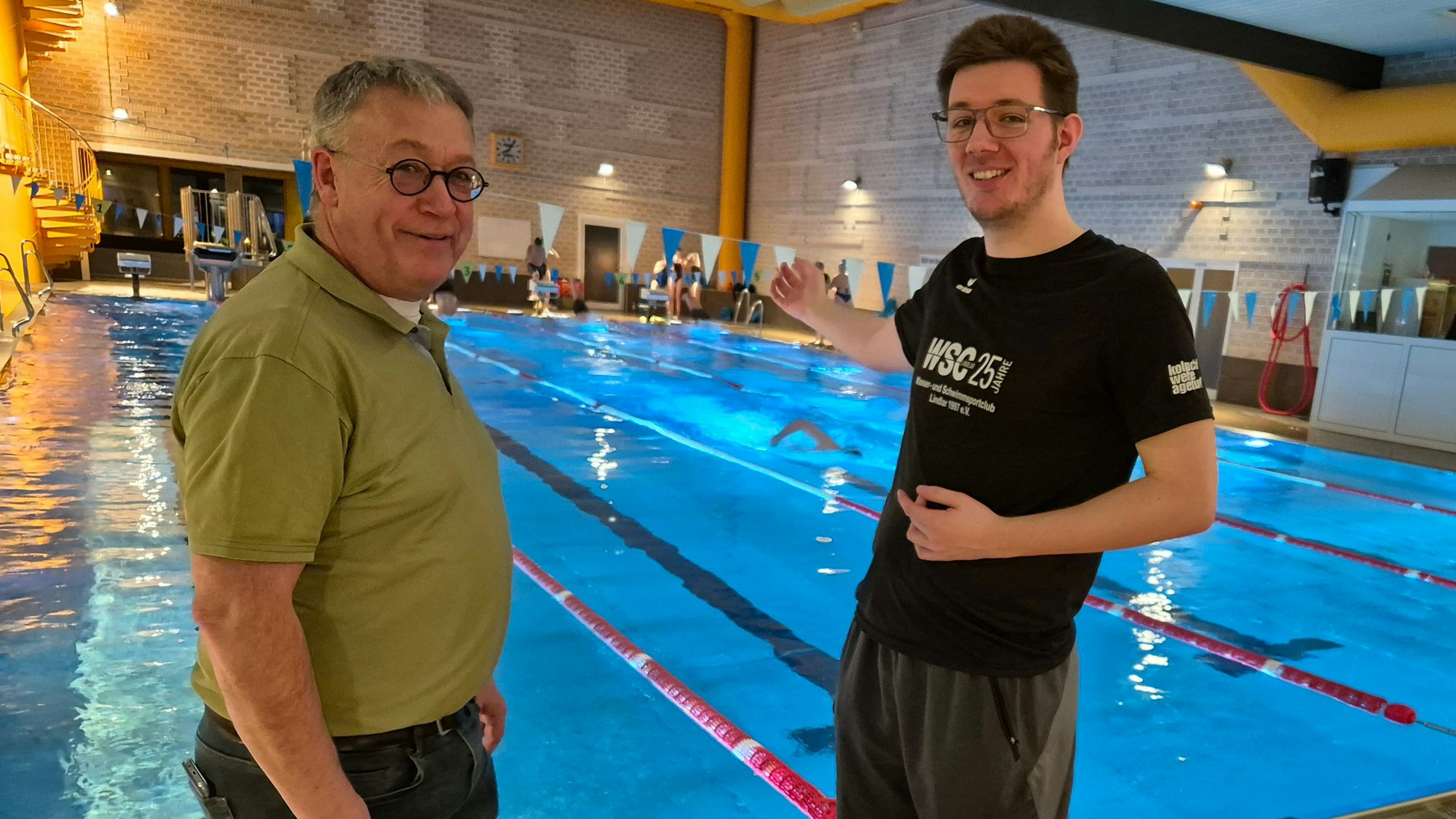 Bild von zwei Männern, im Hintergrund ein Schwimmbecken