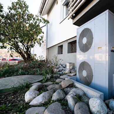 Die Lüftungsanlage einer Wärmepumpe steht vor einem Wohnhaus.