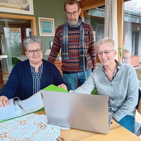 Drei Personen blicken auf einen Laptop.