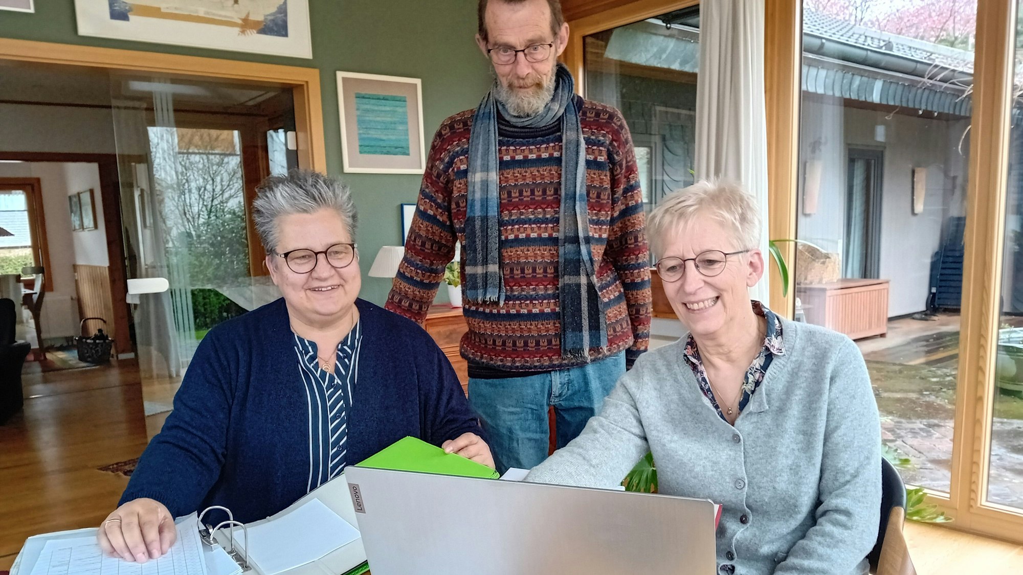 Drei Personen blicken auf einen Laptop.