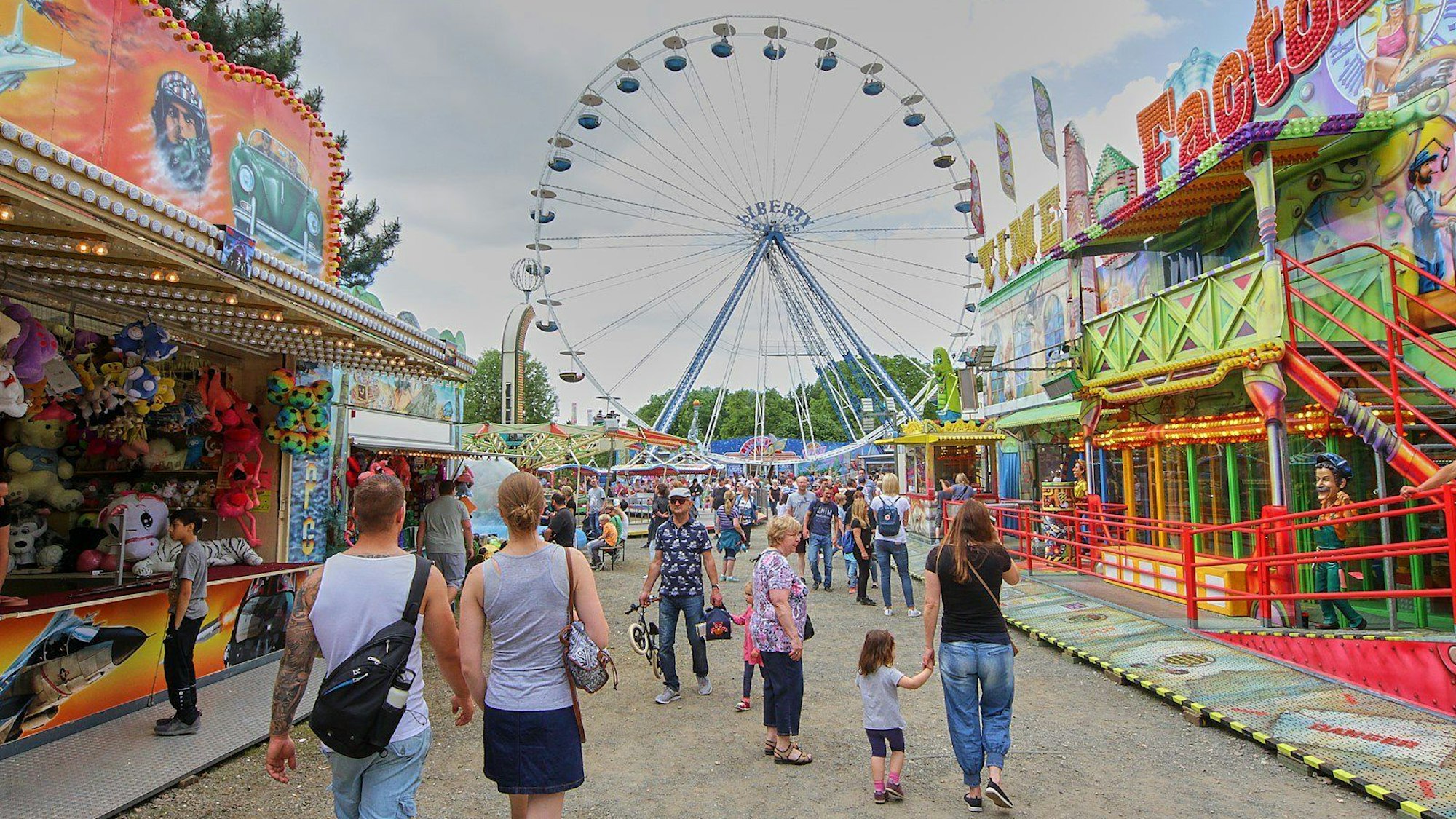 Menschen laufen über das Inselfest. Ein Riesenrad und verschiedene Kirmesbuden und Fahrgeschäfte stehen an den Seiten.