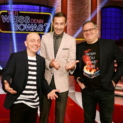 Moderator Kai Pflaume (M.) steht gemeinsam mit Elton (rechts) und Bernhard Hoëcker vor dem Logo der ARD-Quizshow „Wer weiß denn sowas?“.