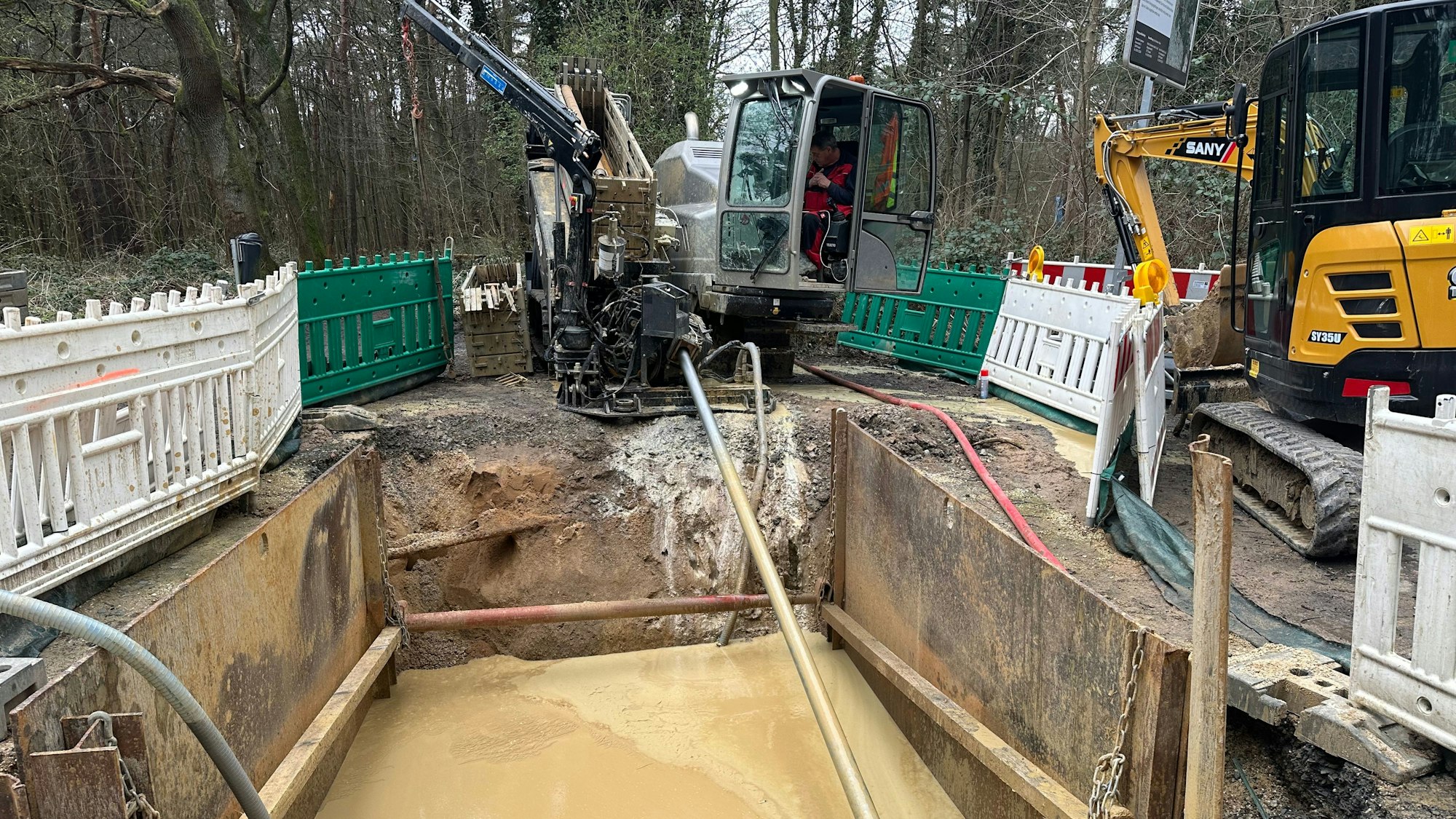 Eine Baugrube, in der Wasser steht. Darum herum stehen kleine Bagger.
