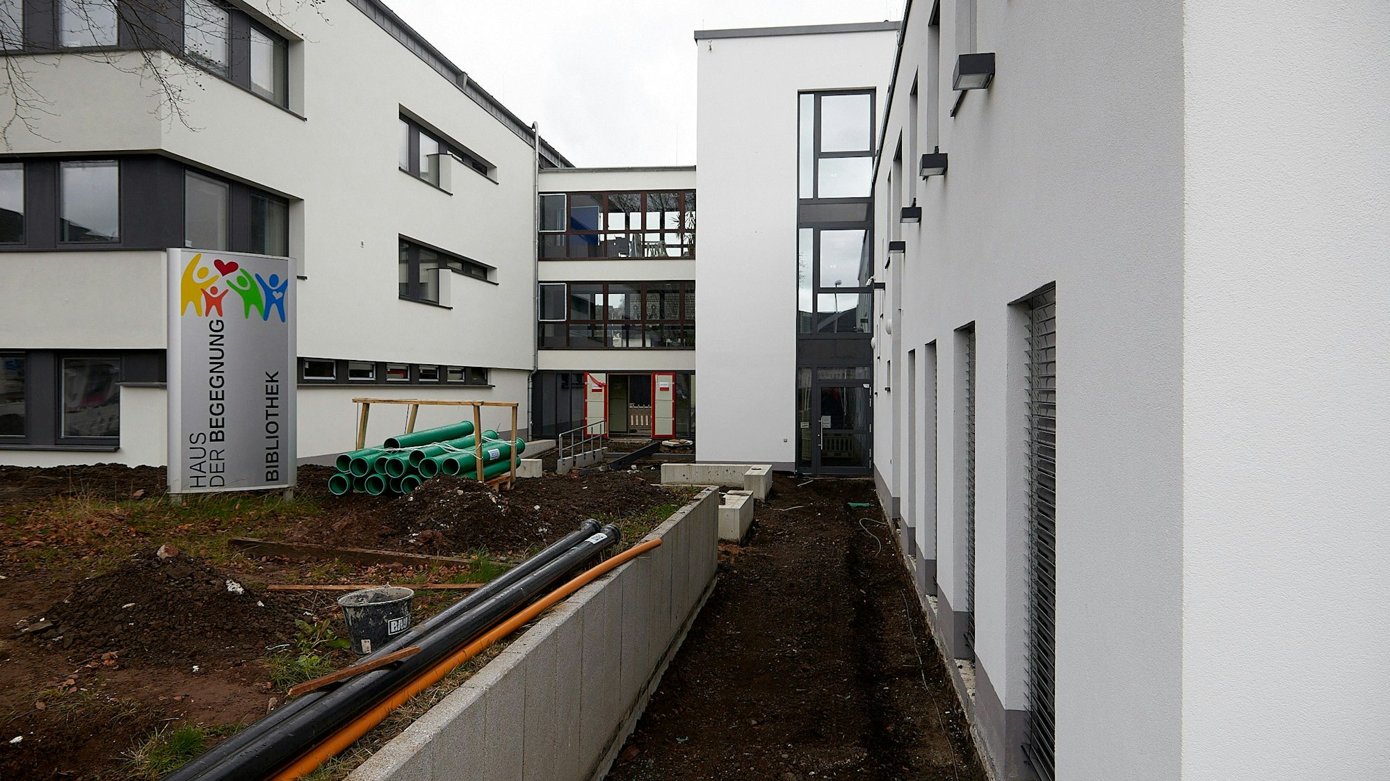 Das Gebäude ist fertig, ein Schild mit der Aufschrift „Haus der Begegnung“ steht auch schon da. Allerdings ist der übrige Außenbereich noch eine Baustelle.