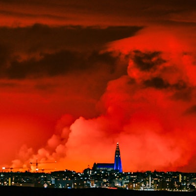 Die Skyline von Reykjavik ist vor dem Hintergrund eines orangefarbenen Himmels zu sehen, der durch geschmolzene Lava entstanden ist, die am 16. März 2024 aus einer Spalte auf der Halbinsel Reykjanes nördlich der evakuierten Stadt Grindavik im Westen Islands ausströmt.