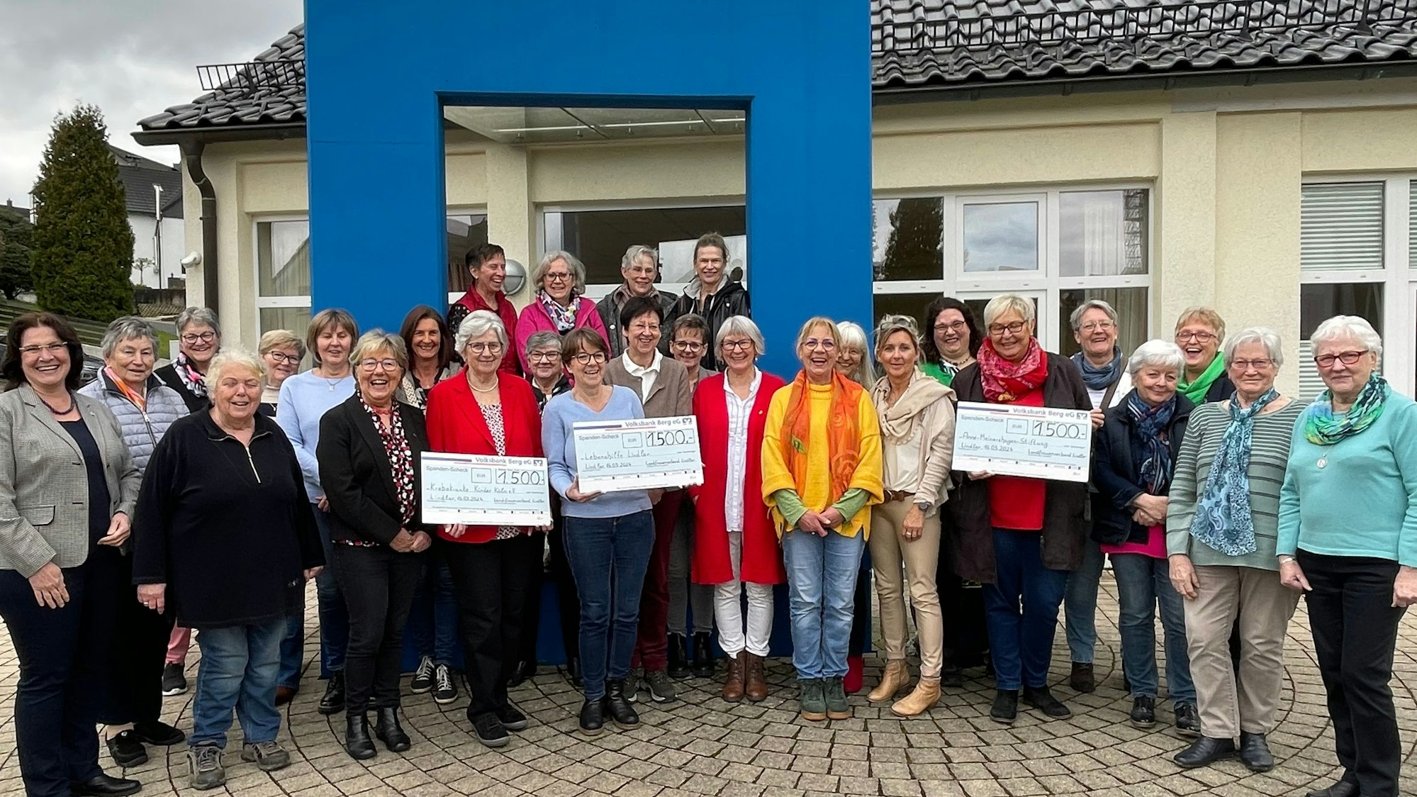 Eine große Gruppe Frauen steht zusammen. Sie halten drei Spendenschecks in den Händen.