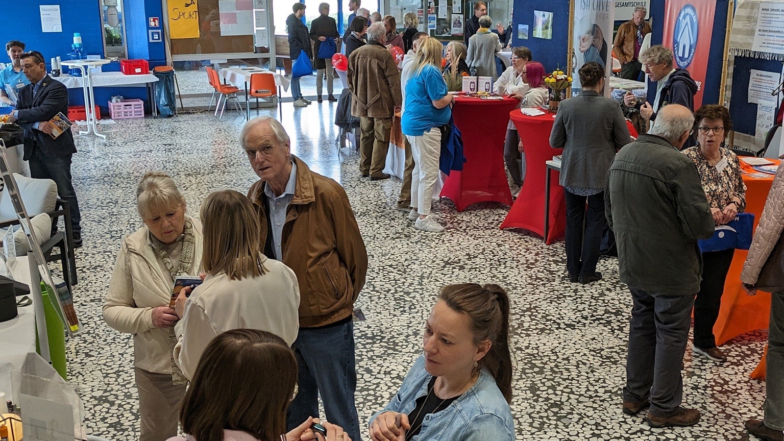 Menschen lassen sich in der Aula der Gesamtschule an Ständen beraten.