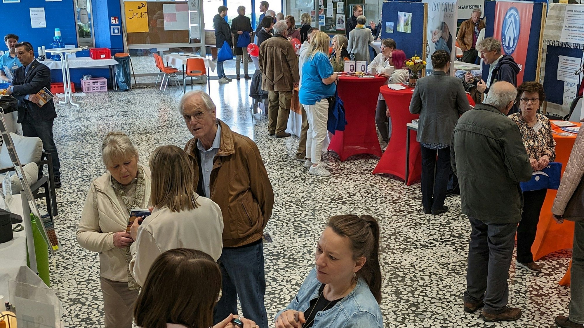 Menschen lassen sich in der Aula der Gesamtschule an Ständen beraten.