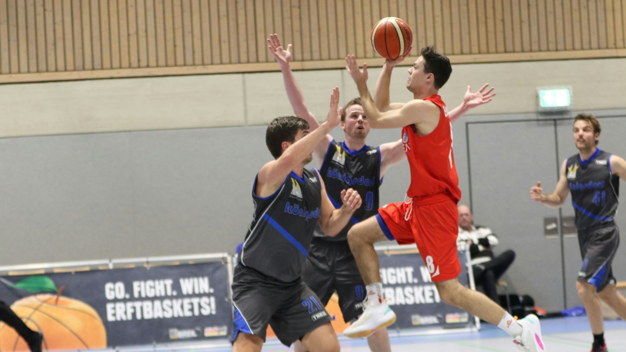 Julian Cziraky ist mit dem Ball in der Hand aus dem Lauf heraus in Richtung Korb abgesprungen. Zwei Gegenspieler haben die Arme zum Block in die Höhe gereckt.
