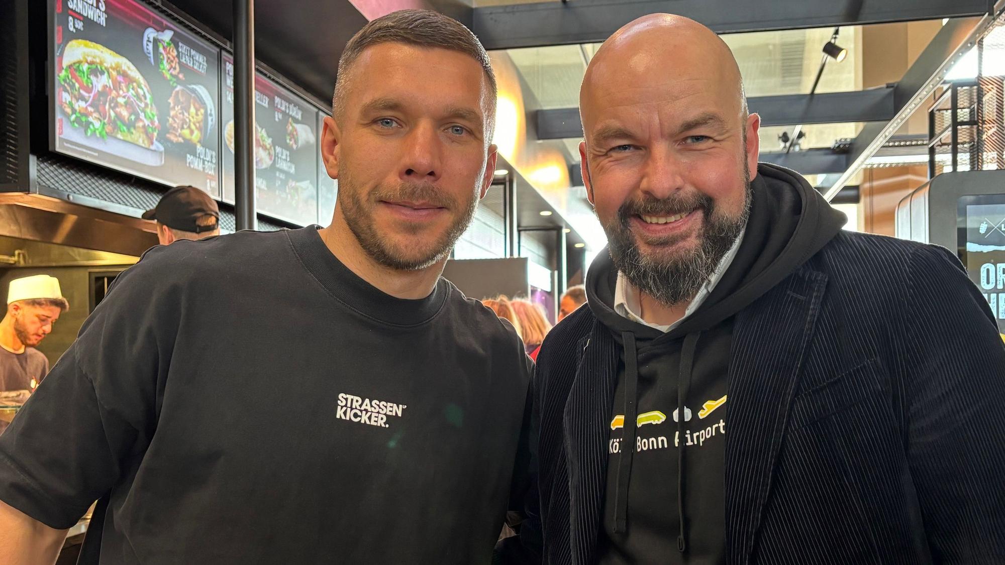 Thilo Schmid, Vorsitzender der Geschäftsführung der Flughafen Köln/Bonn GmbH freut sich mit Lukas Podolski über die neue Mangal-Döner Filiale.