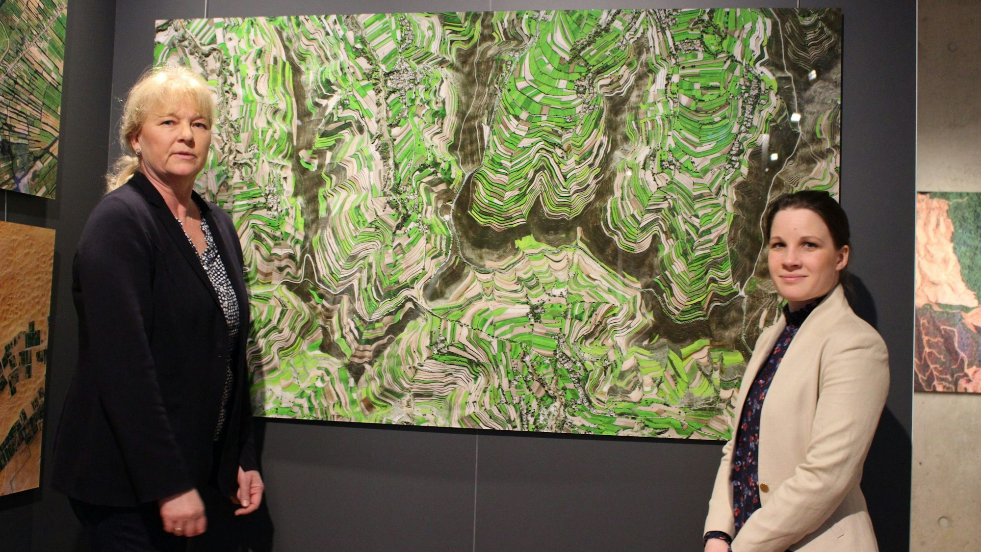 Dr. Heike Lützenkirchen und Maja Kützemeier stehen vor einem Satellitenbild, das die Terrassen zeigt.