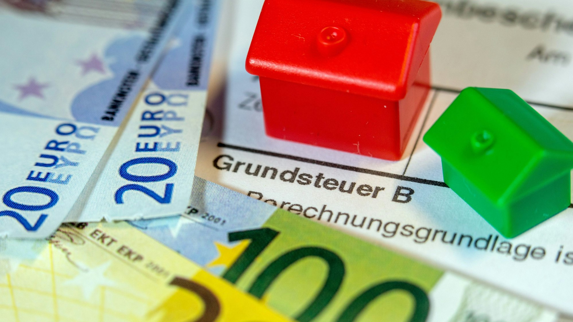 Ein Spielzeughaus und die Nachbildung von Euro-Geldscheinen liegen auf einem Abgabenbescheid für die Entrichtung der Grundsteuer