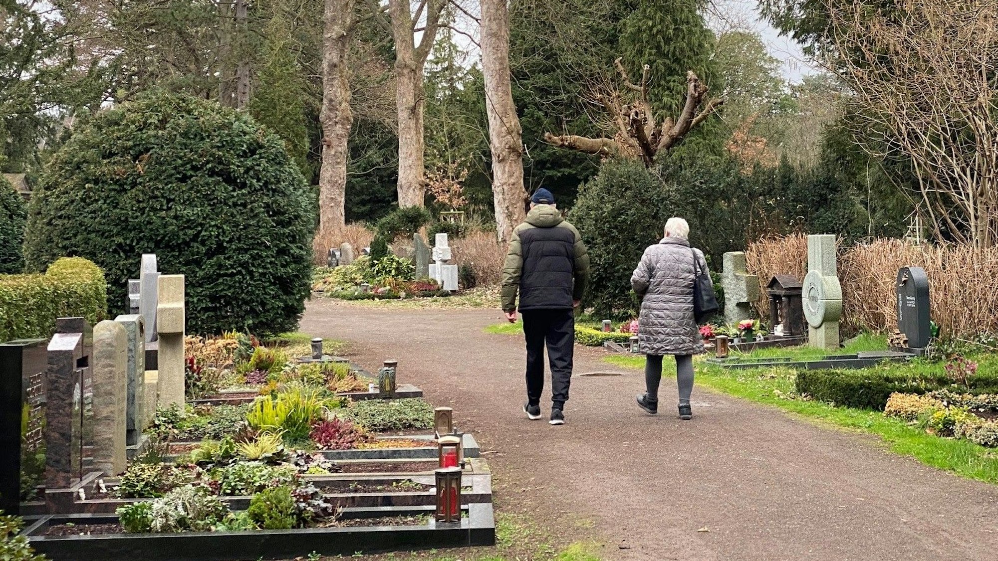 Zu sehen ist der Brühler Südfriedhof mit Grabstätten und zwei Besuchern.