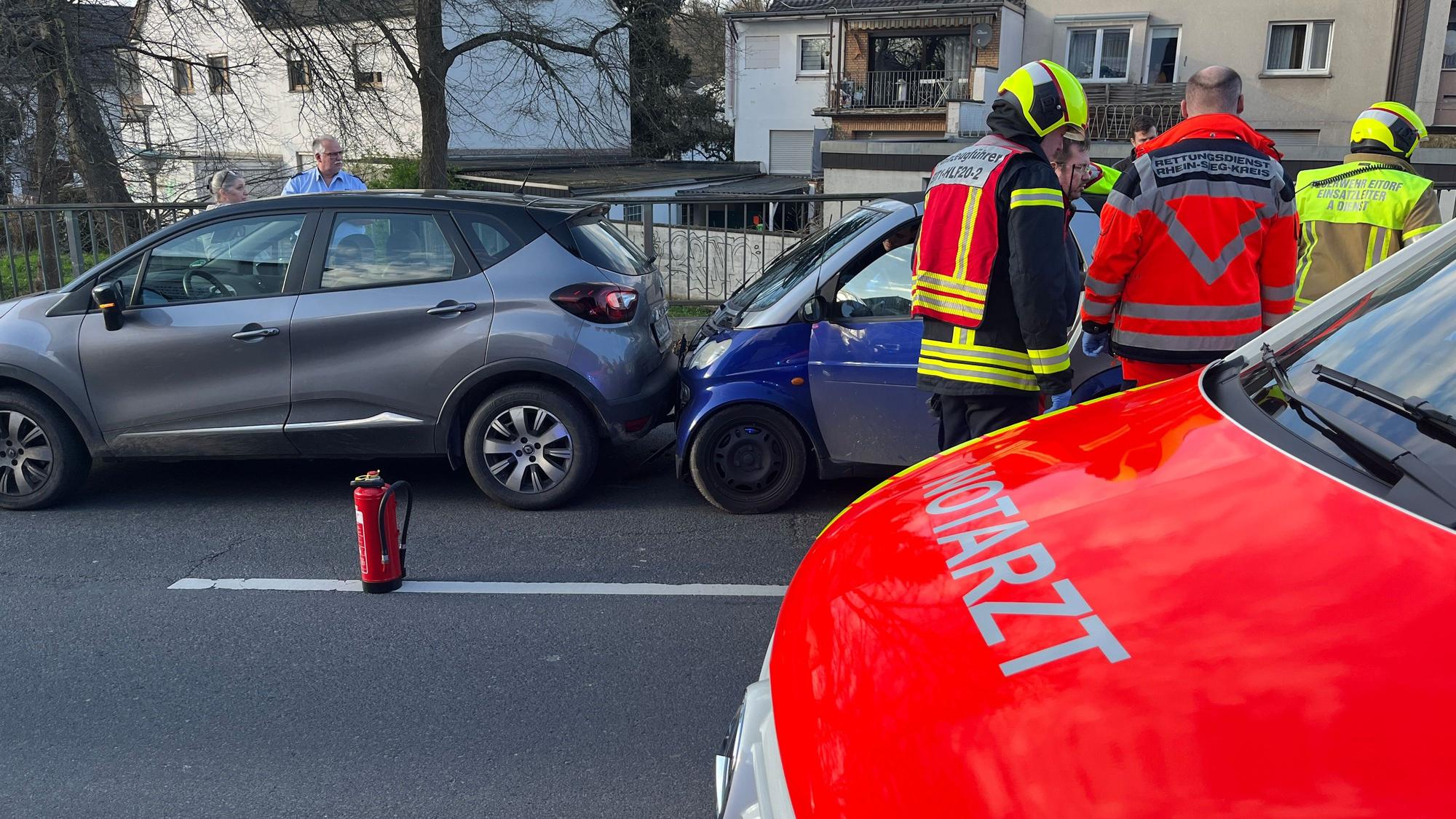 Zwei ineinandergeschobene Kleinwagen stehen auf der Fahrbahn, davor ein Notarztwagen und mehrere Einsatzkräfte.
