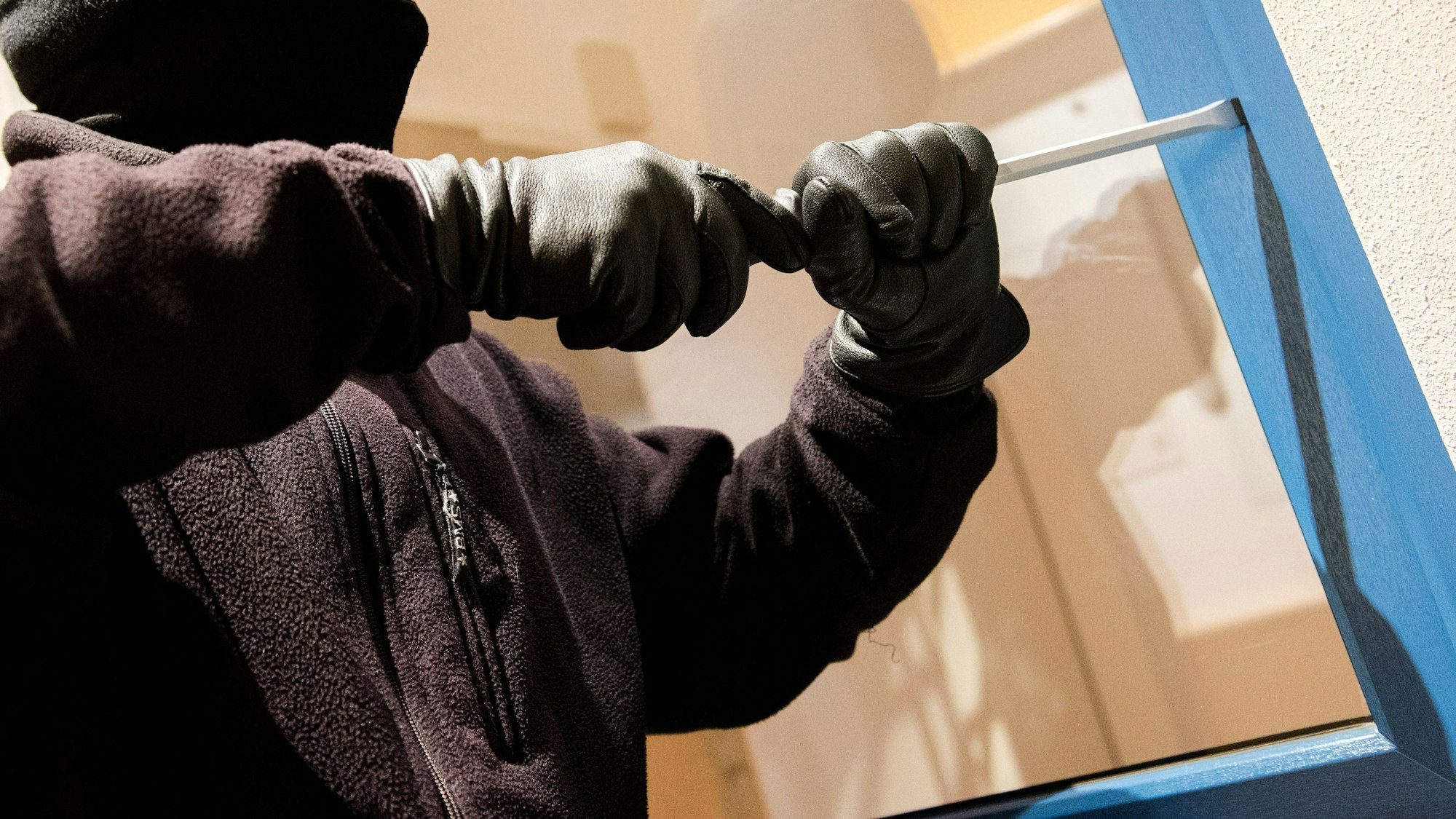 Zu sehen ist ein Einbrecher, der eine Tür aufhebelt.