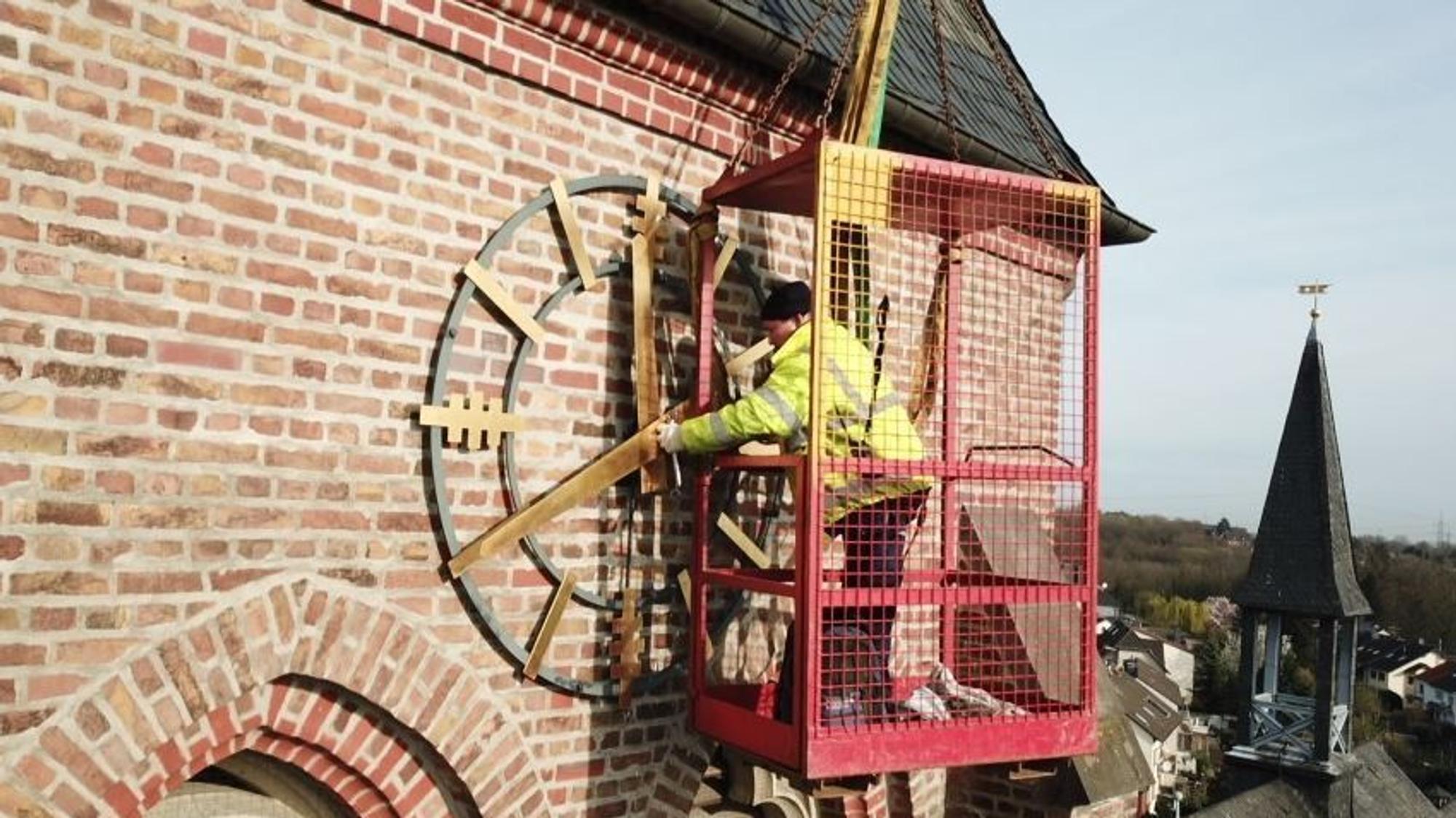 Zu sehen ist ein Arbeiter, der die goldene Kirchturmuhr repariert.