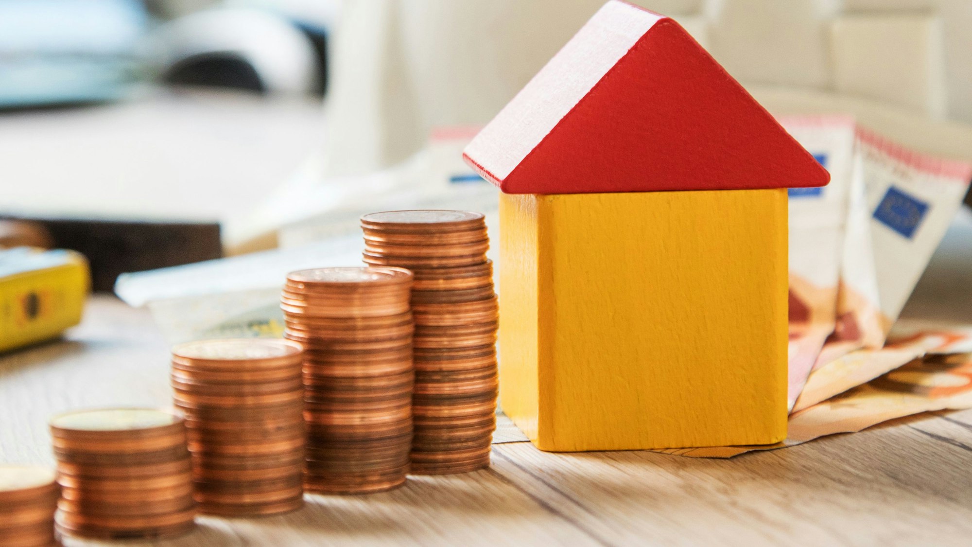 Zu sehen sind ein Miniaturhaus und daneben aufgetürmte Cent-Münzen.