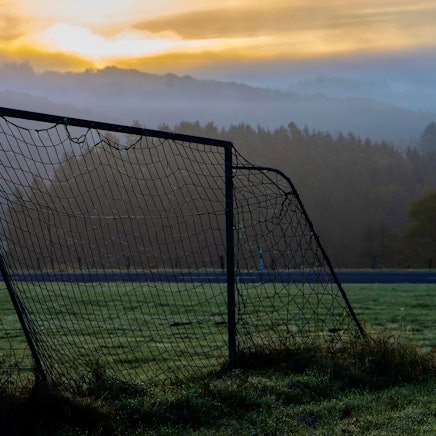 Das Bild zeigt den Bolzplatz zwischen Kolvenbach und Bouderath. Im Hintergrund geht die Sonne auf.