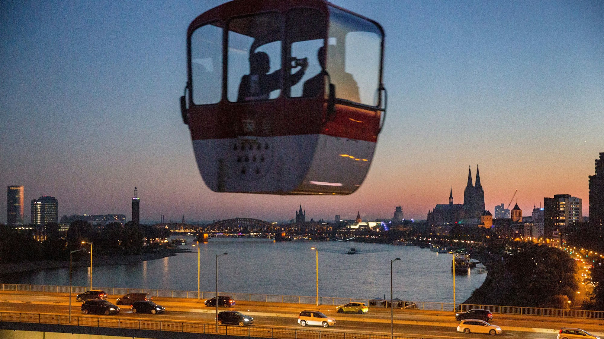 Eine Gondel der Seilbahn vor Köln-Panorama im Sonnenuntergang