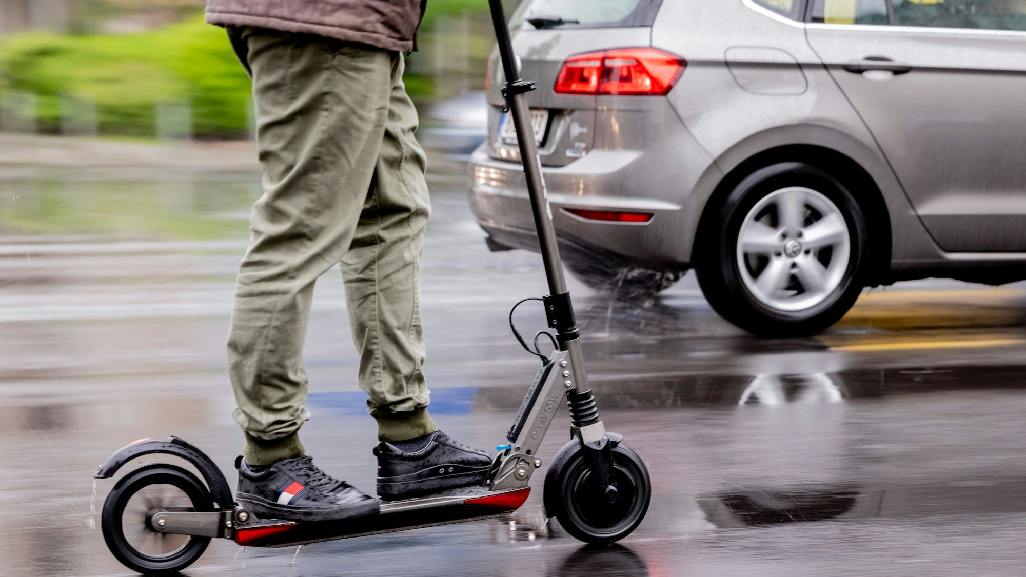 Auf dem Foto sind ein E-Scooterfahrer und ein Auto zu sehen.