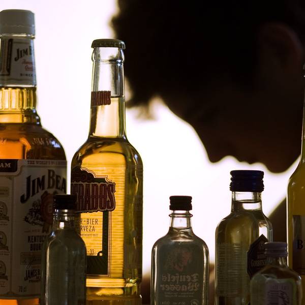 Ein Jugendlicher sitzt hinter Flaschen mit Alkohol,