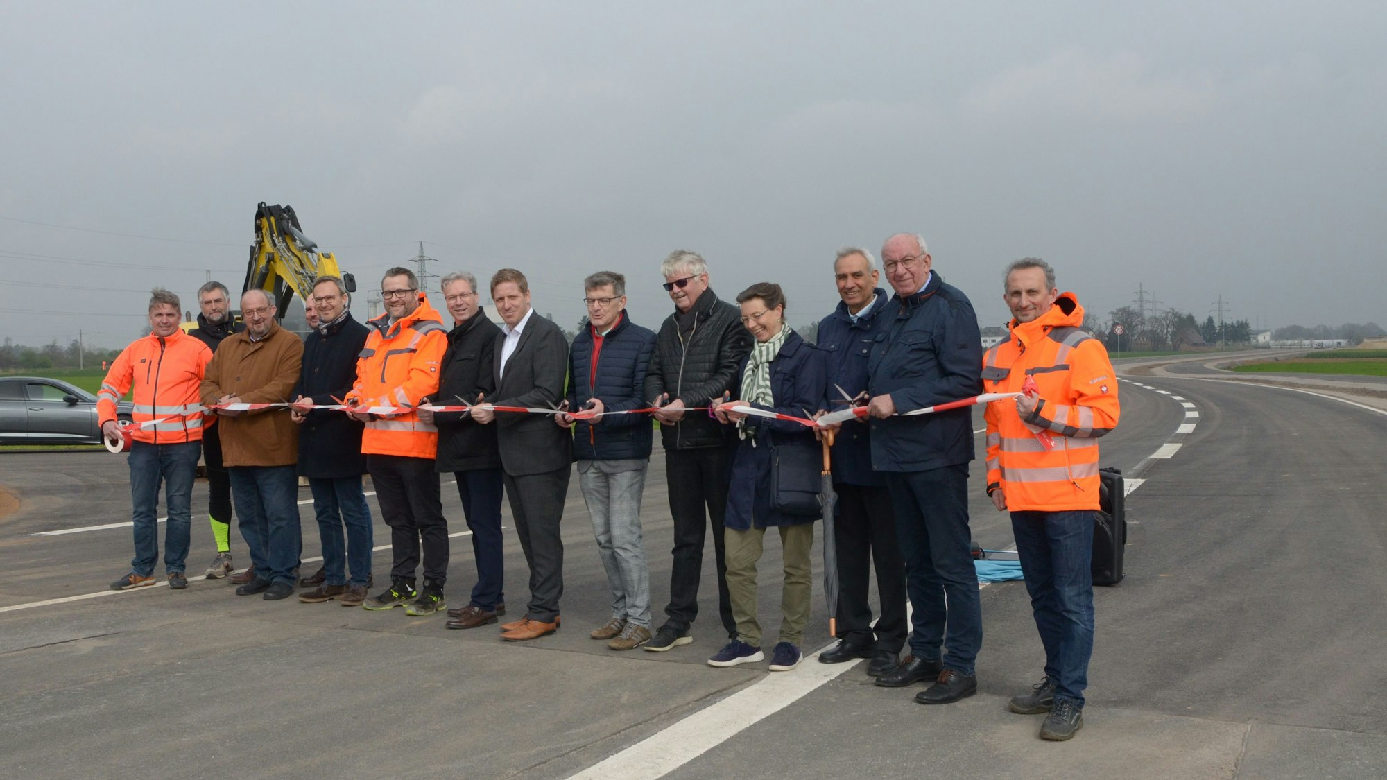Vertreter des Kreises Euskirchen, der Stadt Euskirchen und der beteiligten Unternehmen durchtrennen mit Scheren ein rot-weißes Flatterband. Im Hintergrund ist der Verlauf der Umgehungsstraße erkennbar.