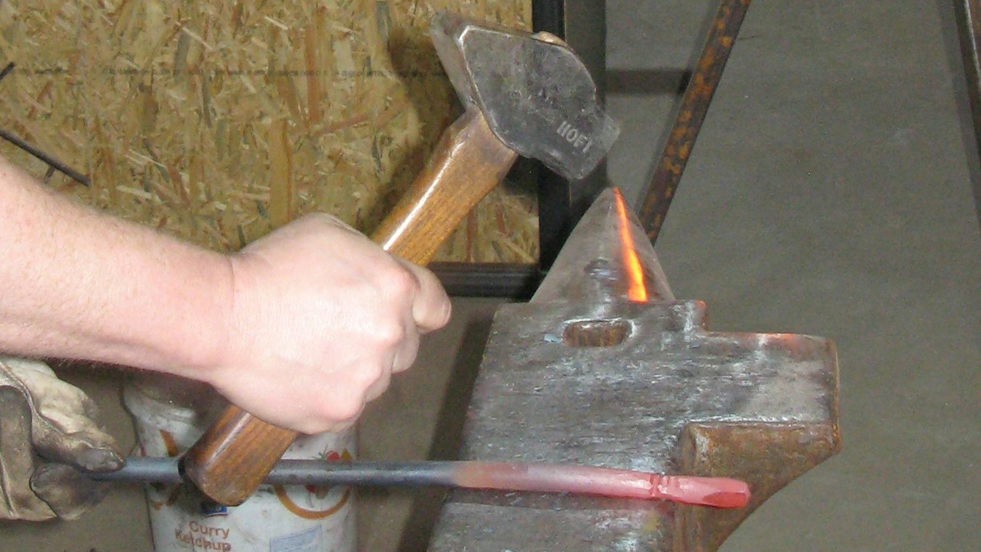 Eine führt einen Schmiedehammer, auf dem Amboss liegt ein glühender Rundstahl.