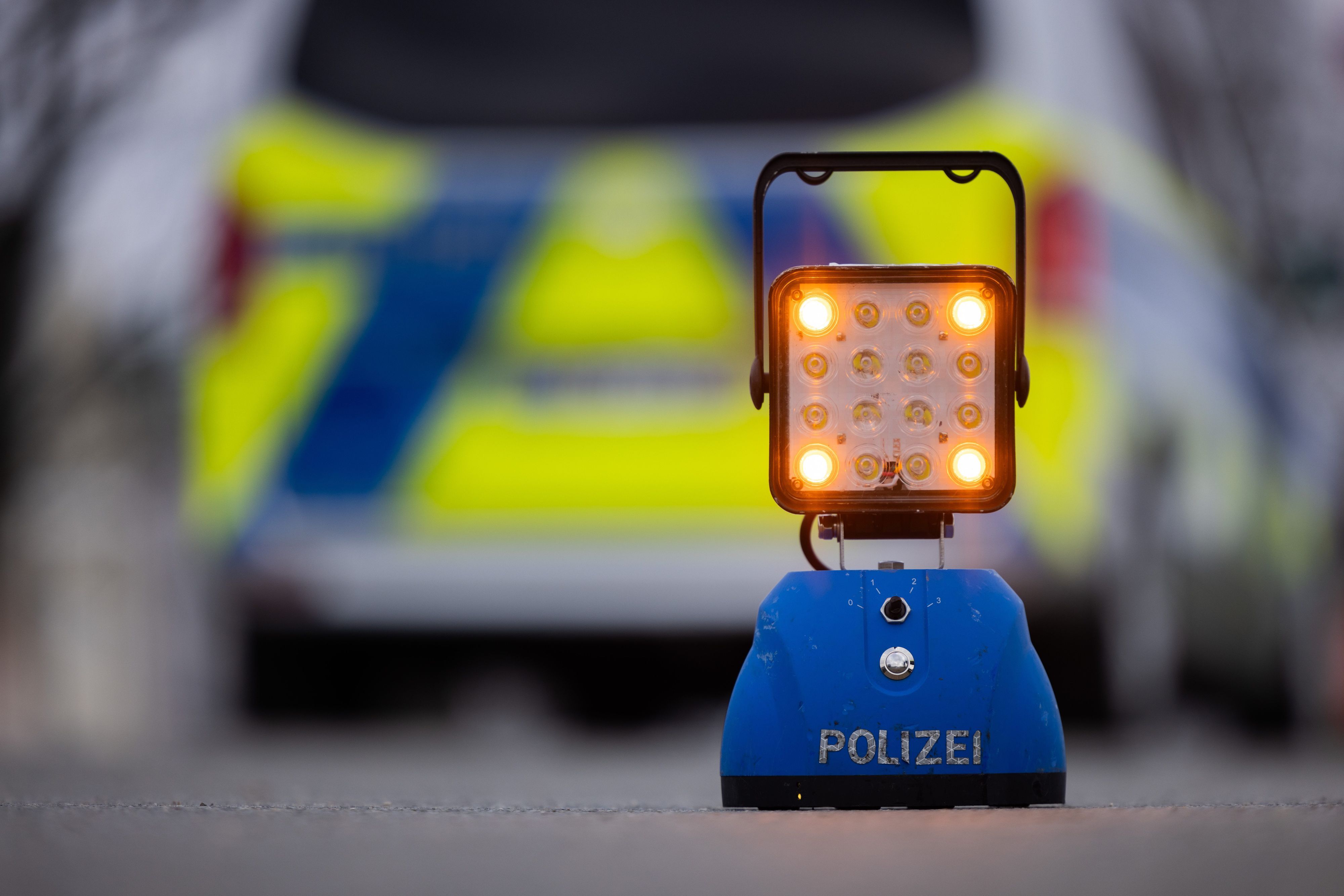 Ein Warnlicht mit der Auschrift „Polizei“ steht auf der Straße vor einem Einsatzfahrzeug der Polizei.