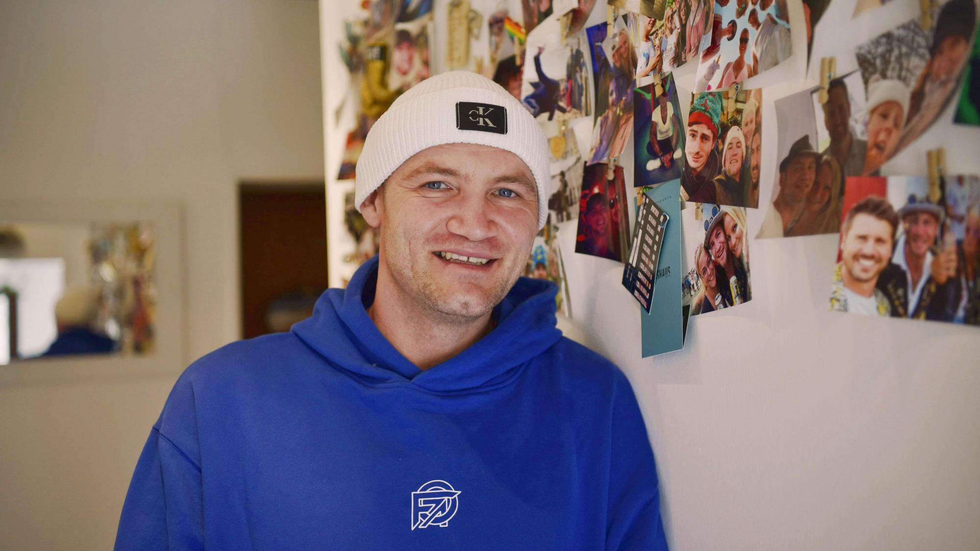 Jan Schepanek steht in seiner Wohnung vor einer Wand mit vielen Fotos, die ihn beim Feiern zeigen.