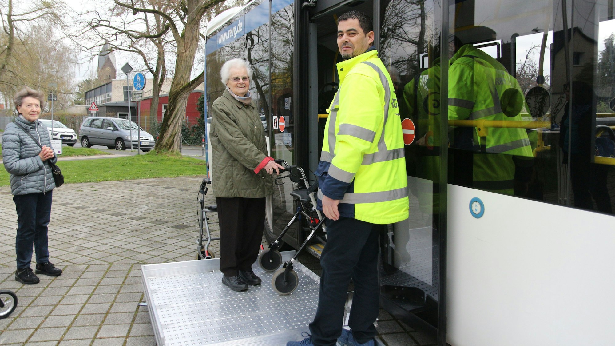 Eine Seniorin übt das Einsteigen in den Bus, neben ihr ein Mitarbeiter der REVG.